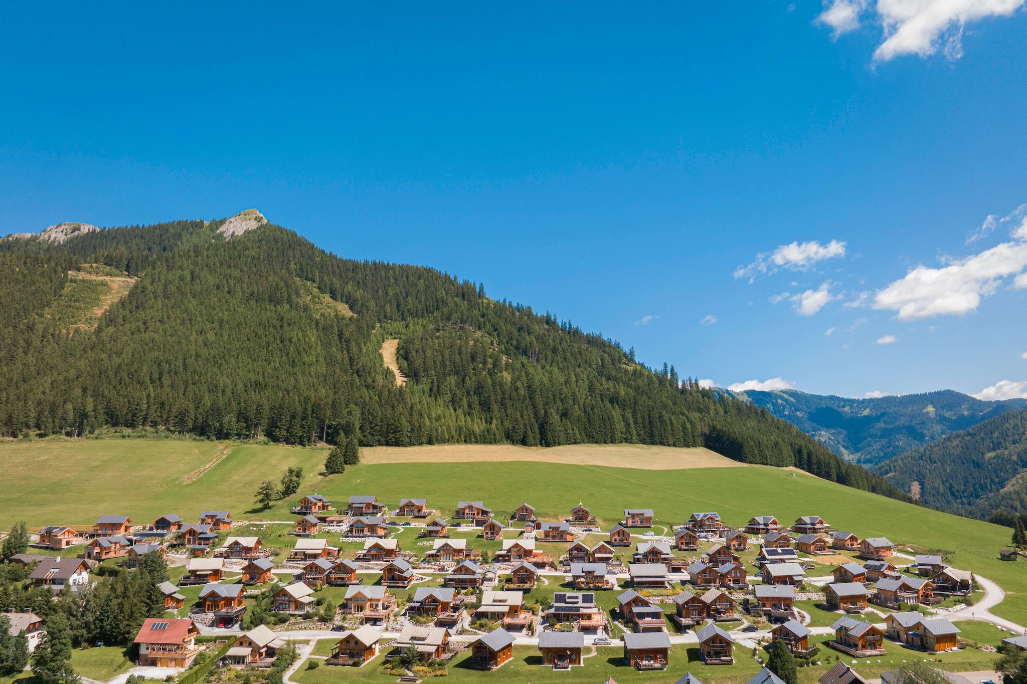 A cluster of log cabins in a mountainous area with a clear sky.