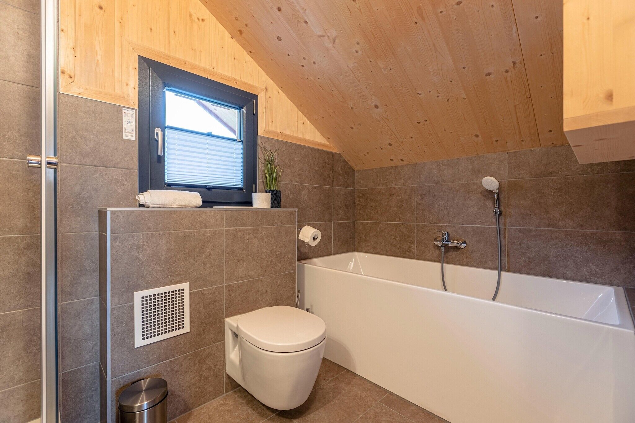 A modern bathroom with a bathtub, toilet, and window.