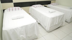 Een hotelkamer met drie eenpersoonsbedden, elk met een witte spreidek en een kussen. Het hoofdeinde heeft een zwart-beige paneelontwerp.