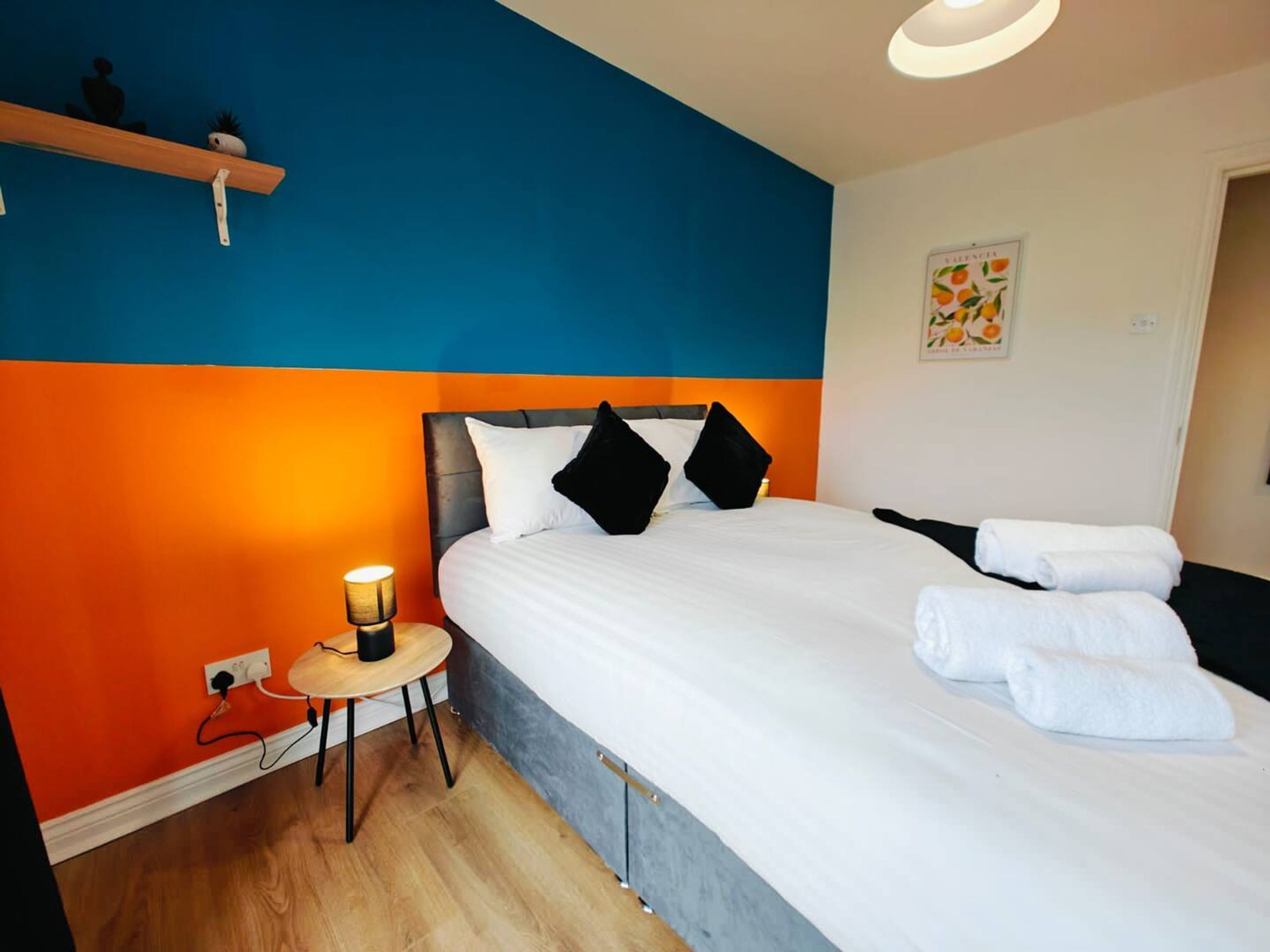 A hotel room with a large bed, a bedside table with a lamp, and a wall with a fruit-themed picture.