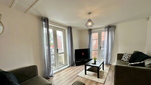A living room with a sofa, a coffee table, a TV, and a hanging light fixture. - 2br City Side Apartment (Belfast)