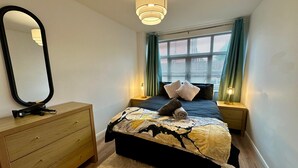 A bedroom with a bed, a dresser, a mirror, and a window with curtains. - 2br City Side Apartment (Belfast)