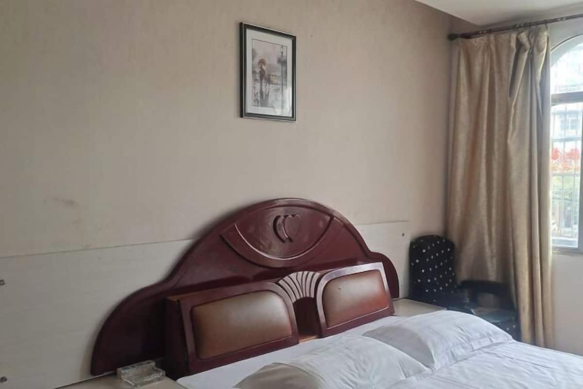 A hotel room with a wooden headboard, a framed picture on the wall, and a window with curtains.