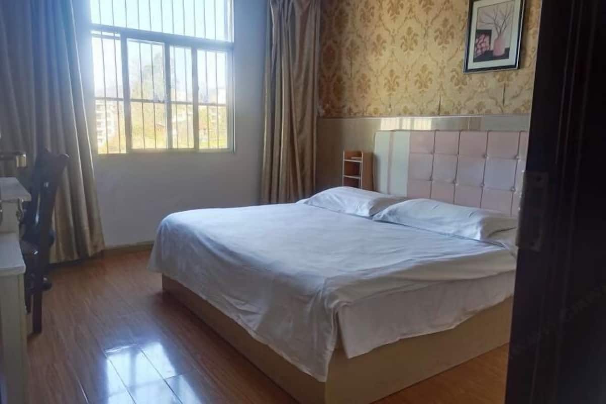 A bedroom with a bed, curtains, a window, and a wall with a framed picture.