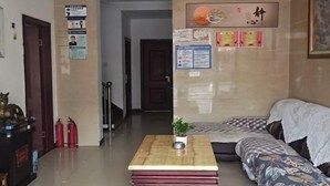 Un hall d’hôtel comprenant un comptoir d’accueil, un canapé, une petite table avec une plante et un mur où sont affichées diverses informations.