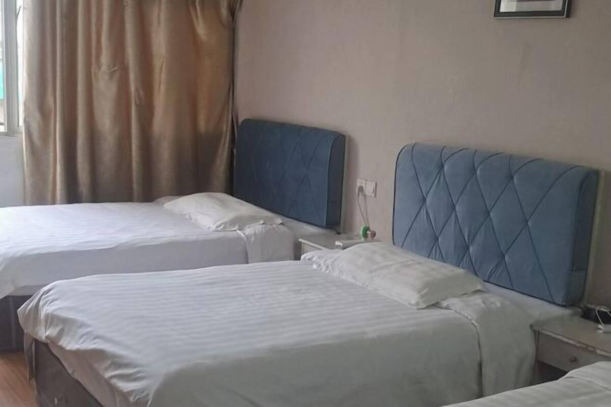 A hotel room with two beds, a window with curtains, and a bedside table with a lamp.