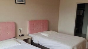 Une chambre d’hôtel avec deux lits, chacun doté d’une tête de lit rose, d’une table de chevet et d’une prise de courant.