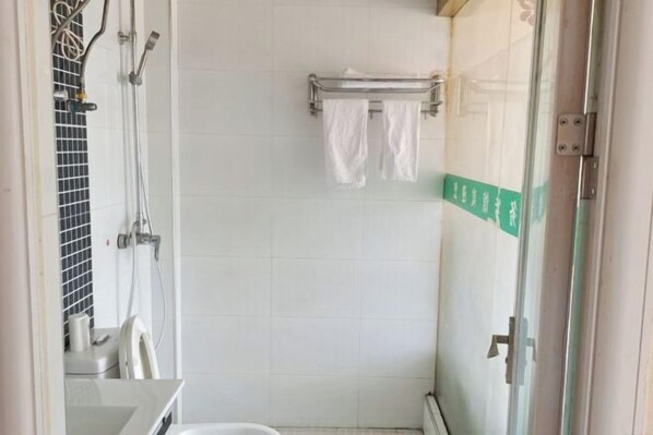 Une salle de bain avec une douche à parois de verre, un porte-serviettes avec deux serviettes blanches et un mur carrelé.