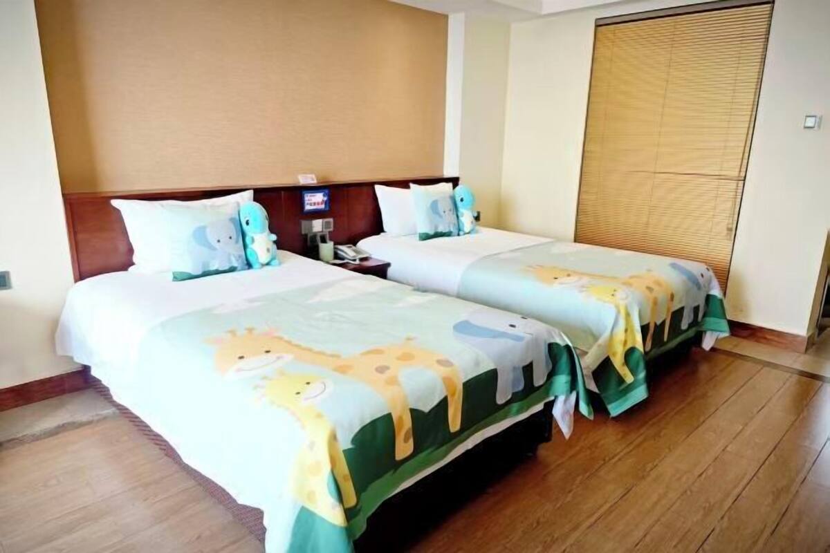 Habitación de hotel con dos camas, cabeceros de madera, un ventanal con persianas y suelo de madera.
