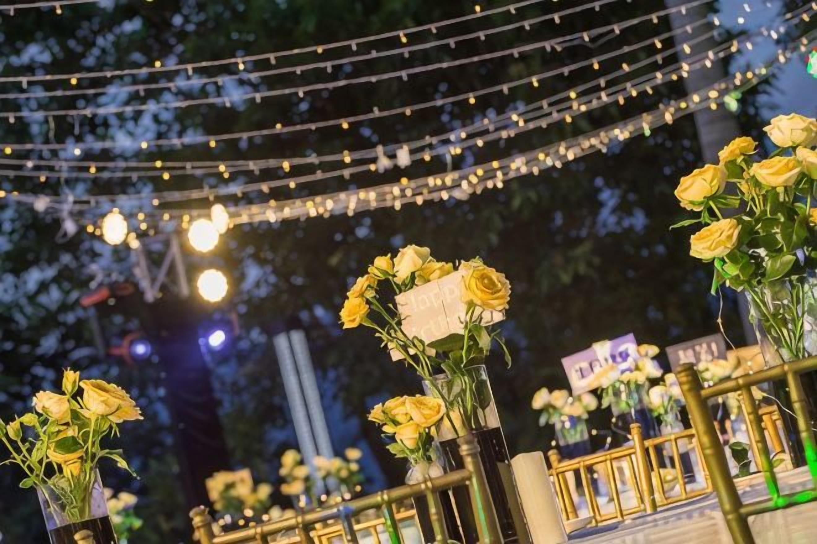 An outdoor setting with string lights and yellow flowers in vases.