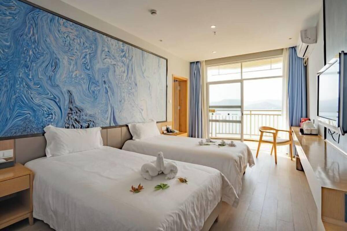 Una habitación de hotel con dos camas, un ventanal con vistas, un escritorio y un televisor.