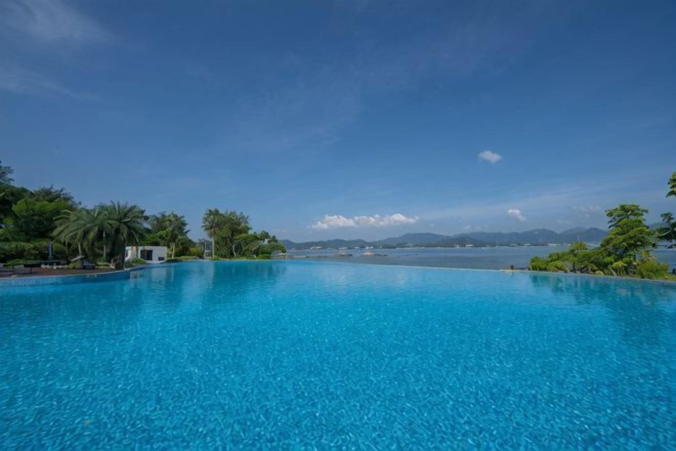 Una piscina azul cristalina con vista al mar y montañas al fondo.