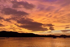 Un coucher de soleil sur une étendue d’eau, avec des reliefs lointains et une série de quais.