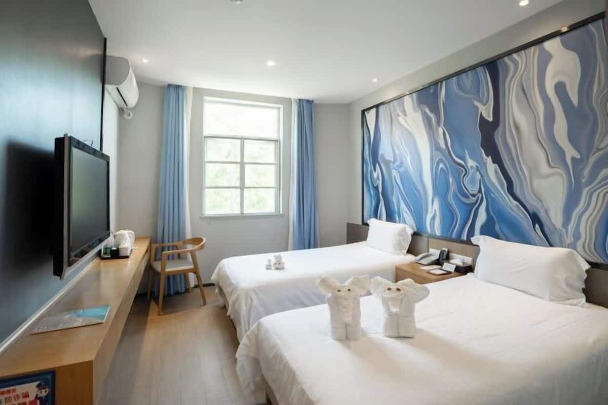 Habitación de hotel con dos camas, un televisor, un escritorio con silla y un cuadro abstracto grande en la pared.