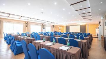 Un salón de conferencias con filas de mesas y sillas, equipado con botellas de agua y blocs de notas.