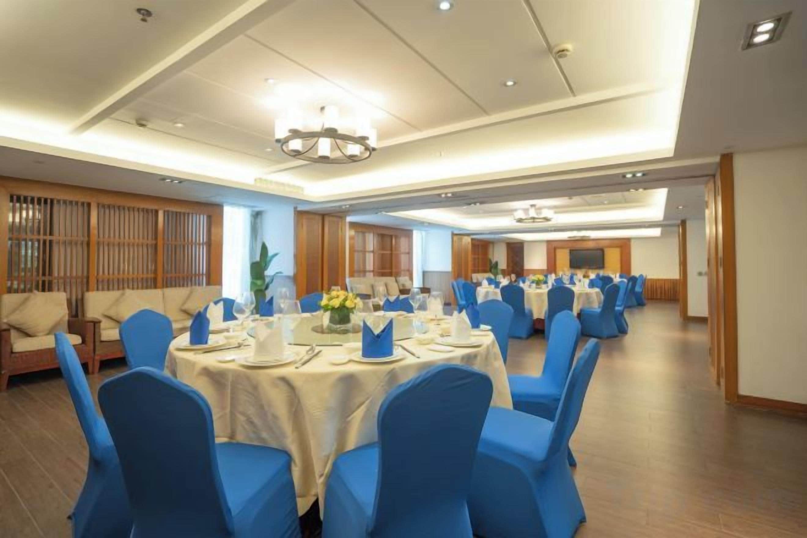 Un salón de banquetes con mesas redondas, sillas azules y una araña de cristal.