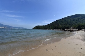 Une plage à l’eau claire, un rivage sablonneux et, en arrière-plan, une colline boisée.