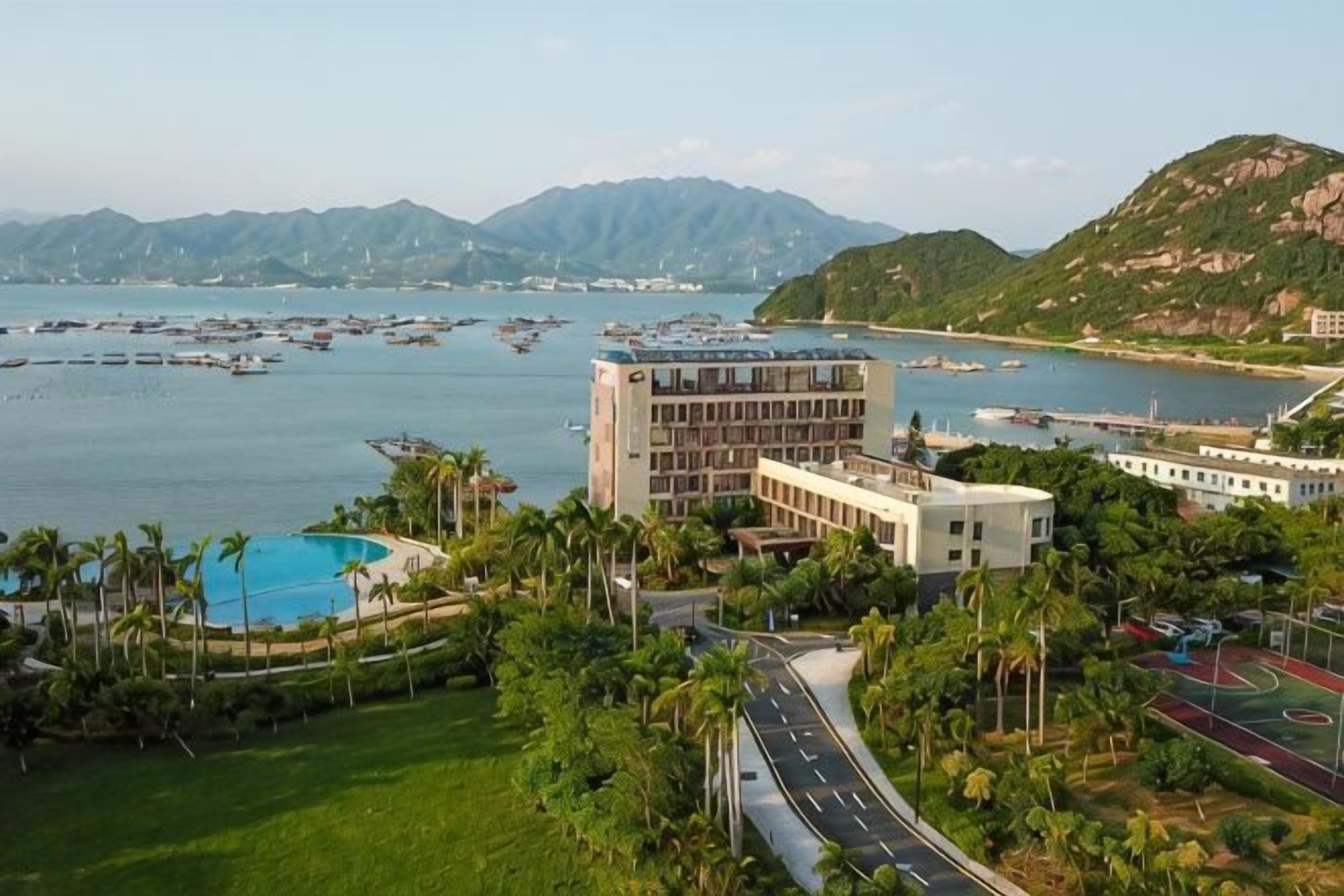 Un hotel costero con piscina, cancha de tenis y vistas al mar y a las montañas.
