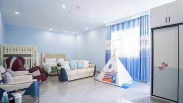 A modern hotel room with a sofa, a bed, a play tent, and a wardrobe.