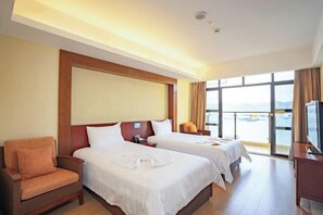 A hotel room with two beds, a sofa, a TV, and a large window with a view.