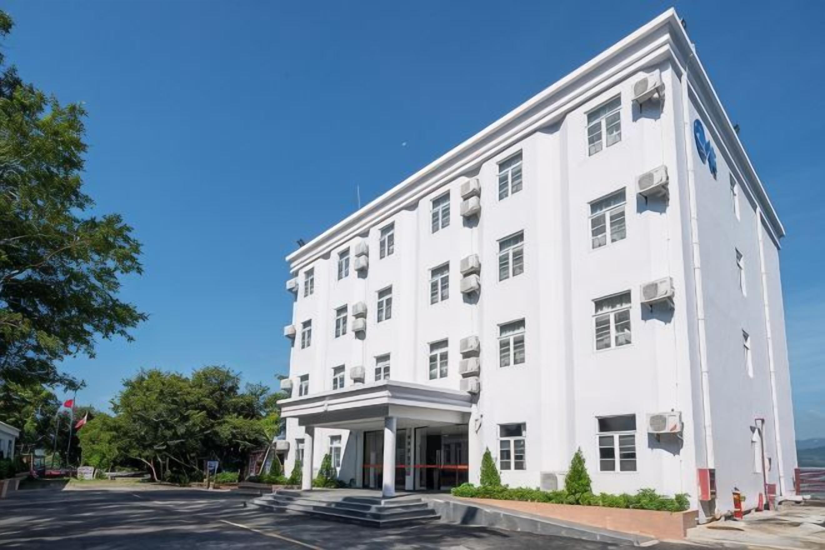 Un edificio blanco con techo plano, múltiples ventanas y una entrada central.