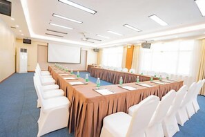 Ein Konferenzraum mit einem langen Tisch, weißen Stühlen und einer Projektionsleinwand.
