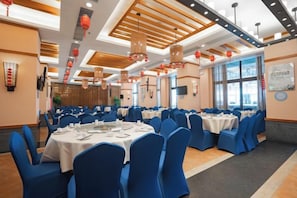 Une salle de banquet avec des tables rondes, des chaises bleues et un plafond en bois.