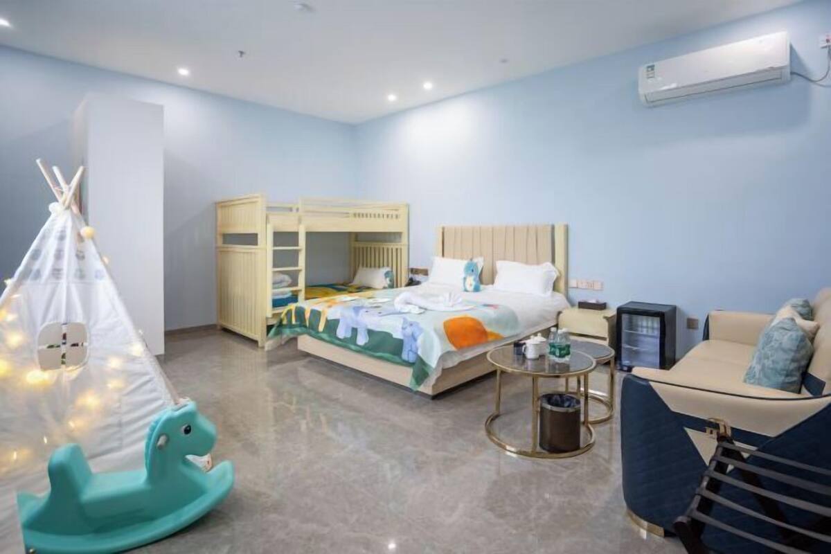 Habitación de hotel para niños con literas, una carpa de juegos, un caballo balancín, un sofá y un televisor.