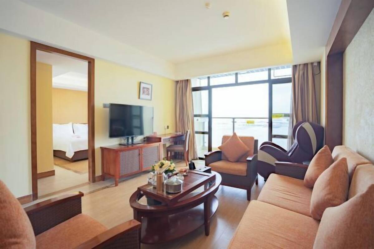Habitación de hotel con sofá, televisor, escritorio con computadora y cama al fondo.