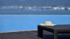 Una terraza de madera con una mesa y un sombrero, con vista a una masa de agua azul cristalina y montañas distantes.