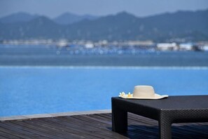 A wooden deck with a table and a hat, overlooking a clear blue body of water and distant mountains. - Dongshan Pearl Island Hotel (Shenzhen)
