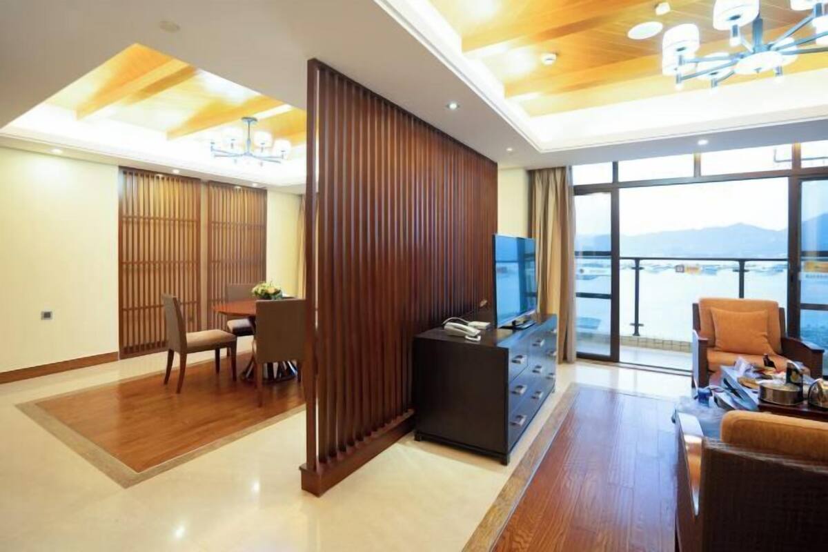 Una habitación de hotel moderna con zona de comedor, televisor y balcón con vistas.