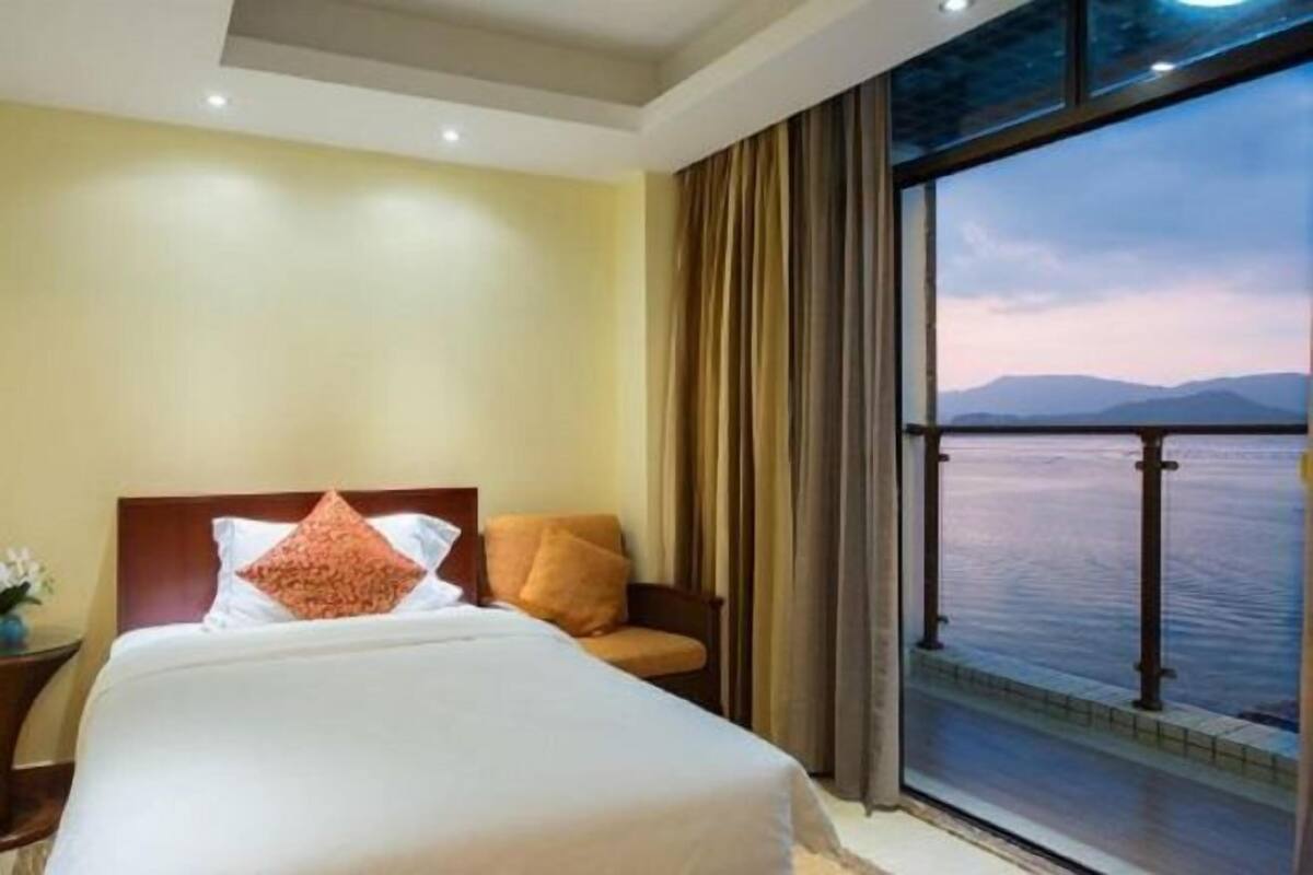 Habitación de hotel con una cama grande, vista al agua y un balcón.