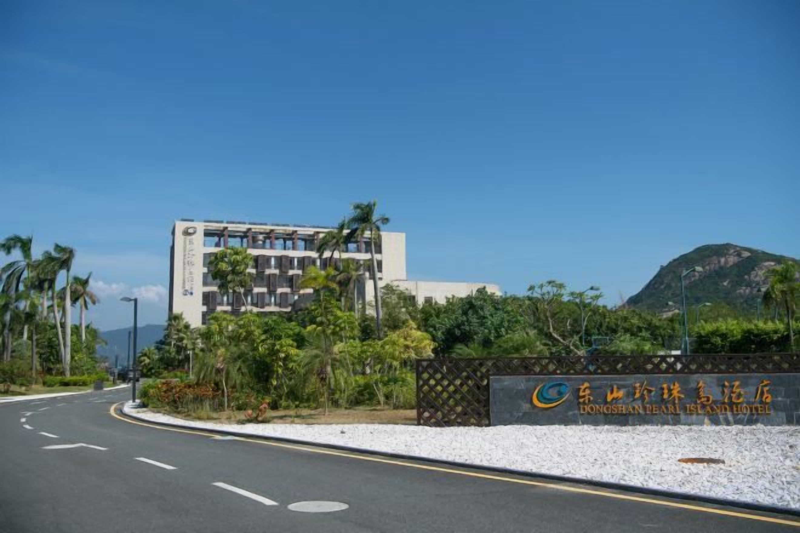 Entrada de hotel con una carretera despejada, un edificio con un letrero y una montaña al fondo.