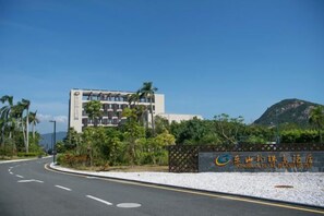 A hotel entrance with a clear road, a building with a sign, and a mountain in the background. - Dongshan Pearl Island Hotel (Shenzhen)