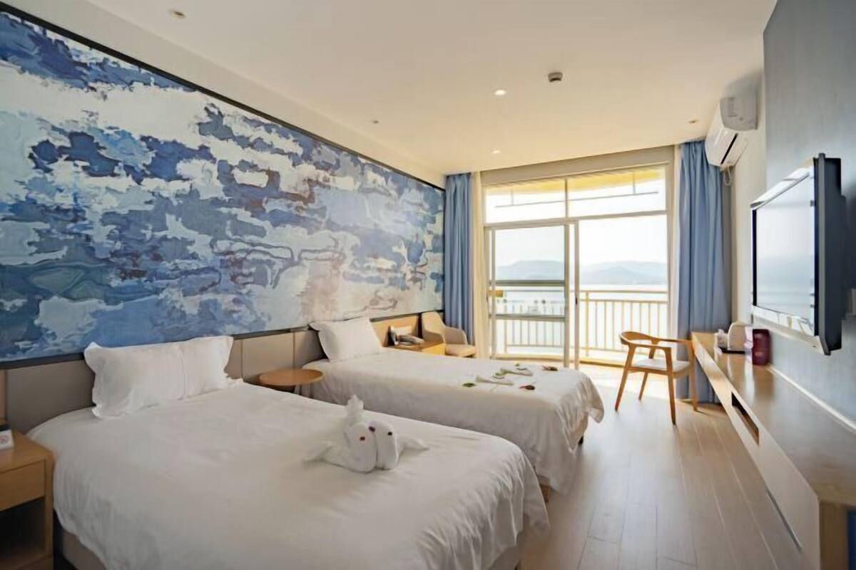 Habitación de hotel con dos camas, un cuadro abstracto grande, un balcón con vistas y un televisor en la pared.