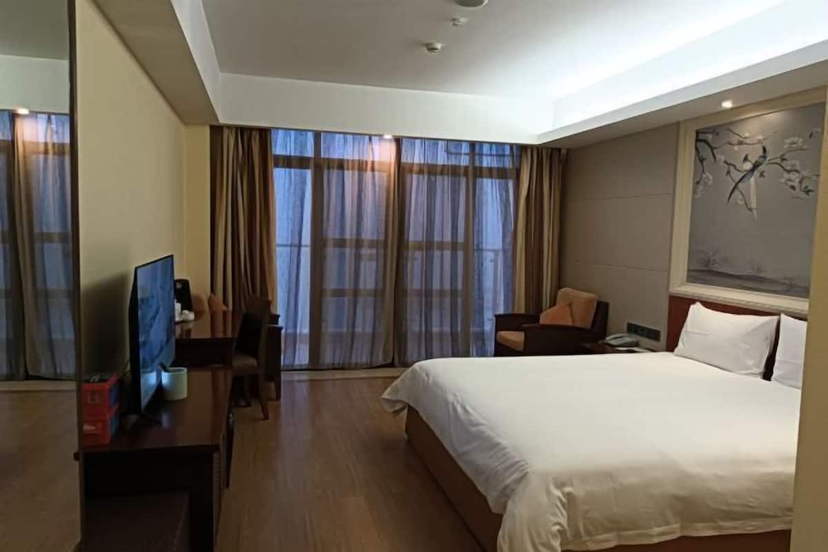 Habitación de hotel con una cama grande, un escritorio con televisor, una silla y un cuadro en la pared.