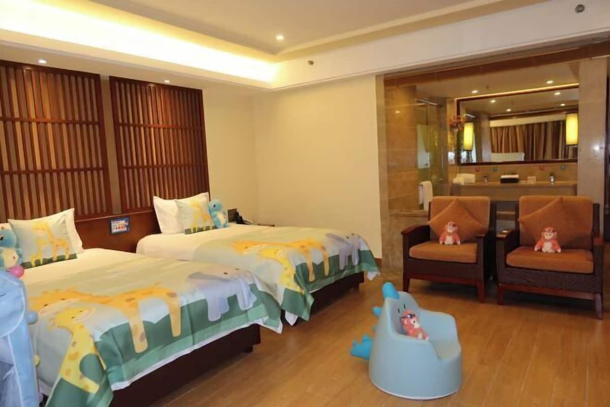 Habitación de hotel con dos camas, una zona de estar con sillones, un pequeño espacio de juegos y un baño con espejo.