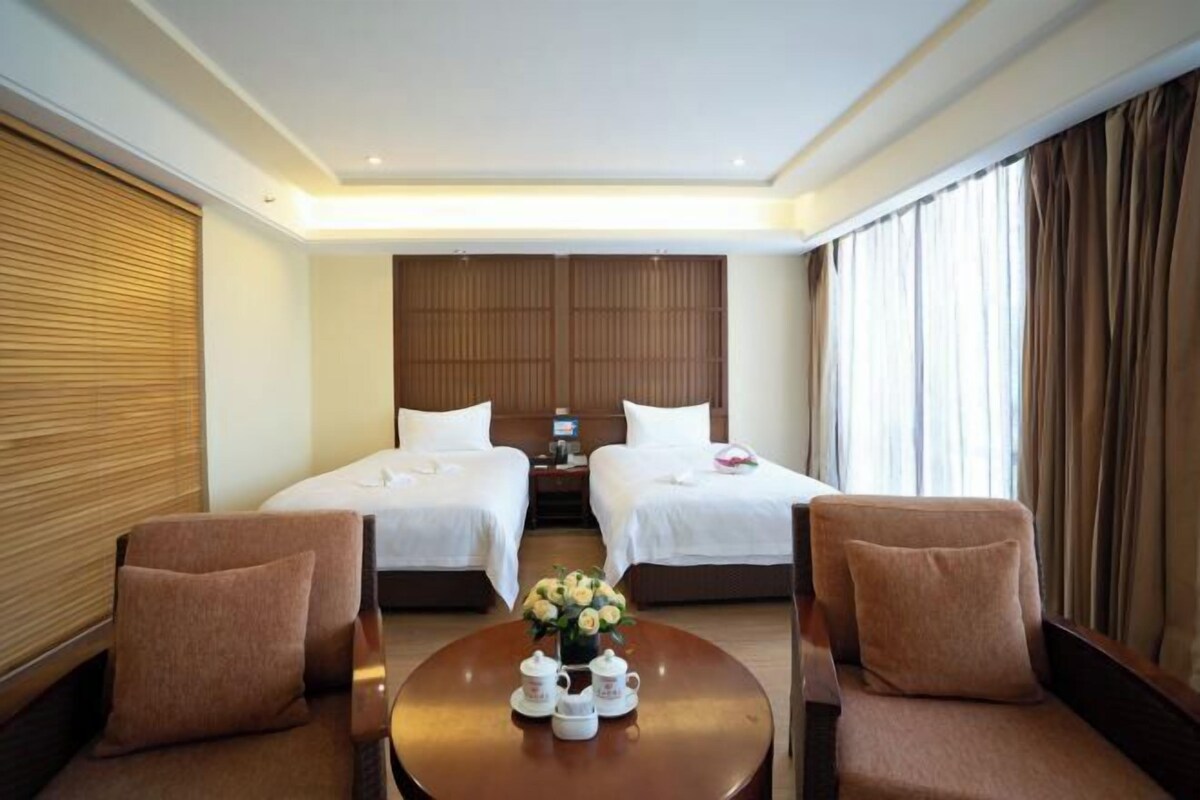 A hotel room with two beds, a small table with a vase of flowers, and two armchairs.