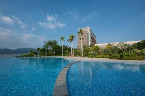 Ein klares, blaues Schwimmbecken mit geschwungener Kante, umgeben von Palmen und einem Gebäude mit weißer Fassade.
