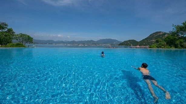 Una piscina con agua azul cristalina, rodeada de vegetación y colinas al fondo.