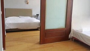 A hotel room with a wooden floor, a bed with white bedding, a wooden door with frosted glass, and a wall-mounted light fixture. - Hai Shi Cheng Lou Business Hotel (Yuhuan)