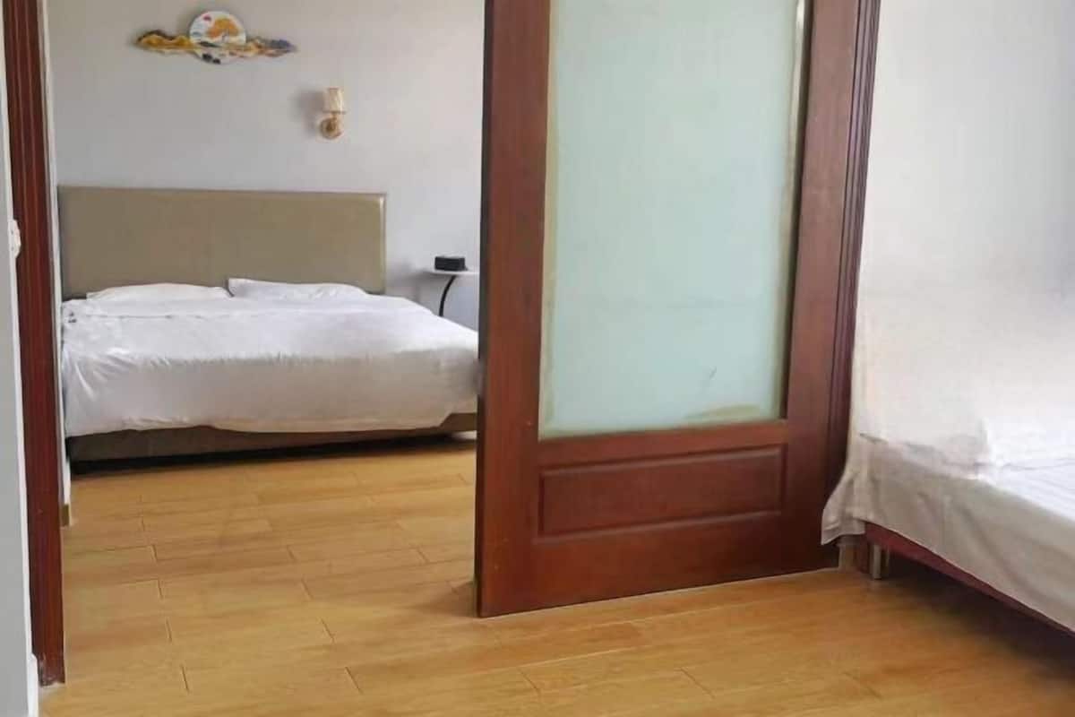 Ein Hotelzimmer mit Holzboden, einem Bett mit weißer Bettwäsche, einer Holztür mit Frostglas und einer wandmontierten Lampe.