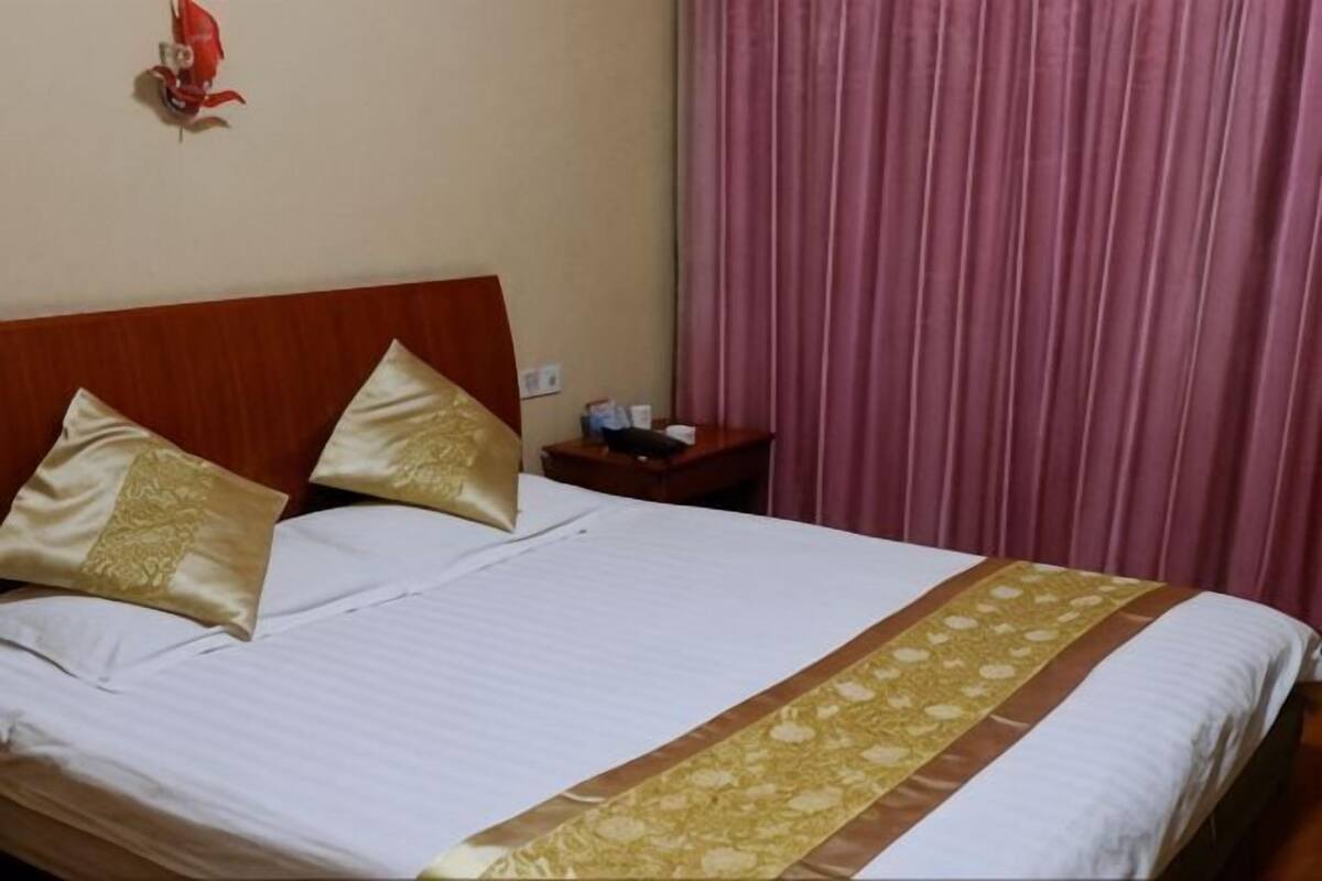 Ein Hotelzimmer mit Bett, Kissen, einem Nachttisch, einem roten dekorativen Gegenstand an der Wand und rosa Vorhängen.