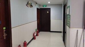 A hallway with a fire extinguisher line, a door with a sign, and a wall-mounted light fixture. - Hai Shi Cheng Lou Business Hotel (Yuhuan)
