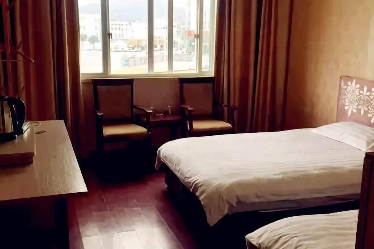 Ein Hotelzimmer mit einem Bett, zwei Stühlen, einem kleinen Tisch und einem Fenster mit Vorhängen.
