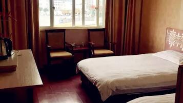 A hotel room with a bed, two chairs, a small table, and a window with curtains.