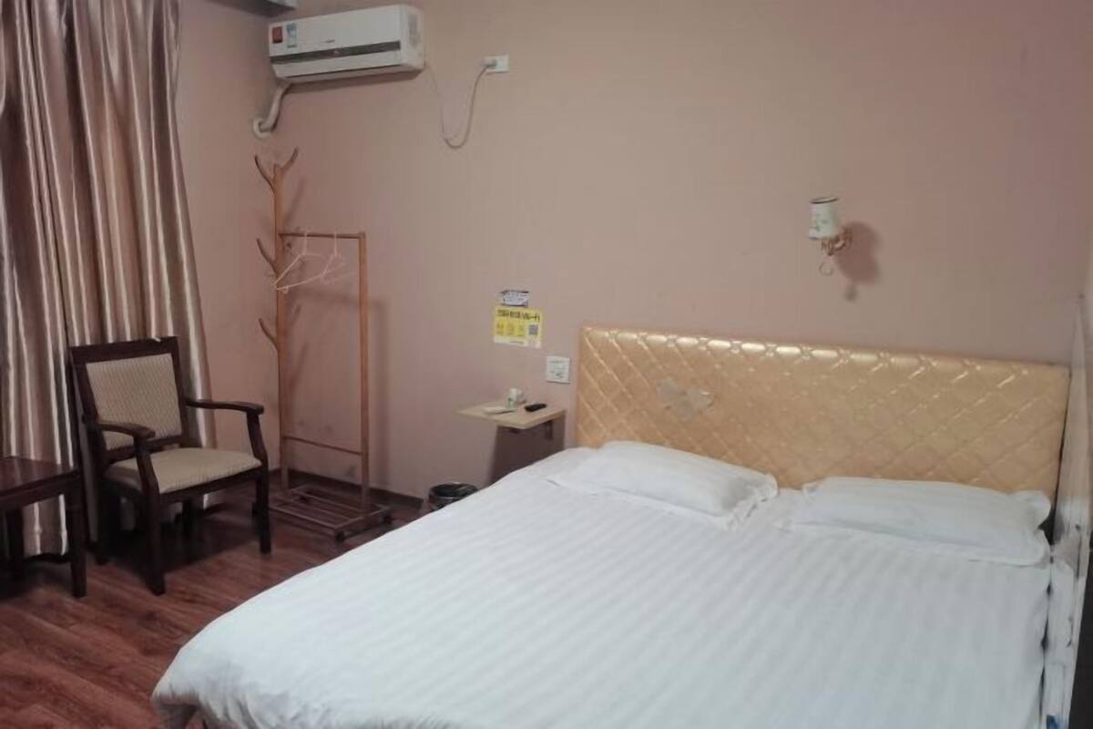 Ein Hotelzimmer mit Bett, Sessel, Kleiderständer, Nachttisch und Klimaanlage.