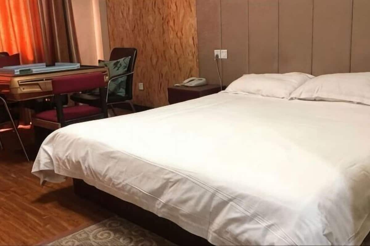 Ein Hotelzimmer mit einem Bett, einem Schreibtisch mit Stuhl, einem Telefon und einer Wand mit strukturierter Oberfläche.