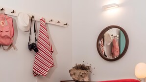 Une pièce comprenant une chaise rouge, une commode en bois, un miroir et un porte-manteau mural sur lequel sont accrochés divers objets.